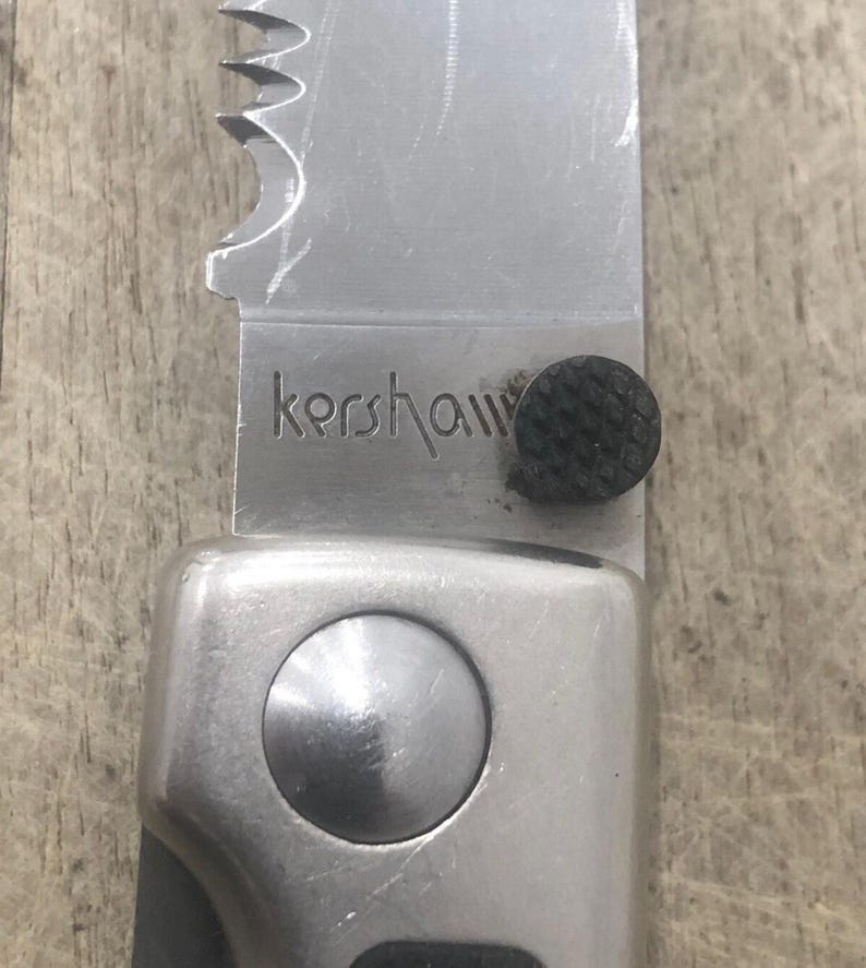 Pode incluir: Close-up de uma faca dobr&aacute;vel prateada com uma l&acirc;mina parcialmente serrilhada. A palavra "kershaw" est&aacute; gravada na l&acirc;mina. A pega &eacute; prateada com uma pega texturizada preta. Uma ferramenta pr&aacute;tica.