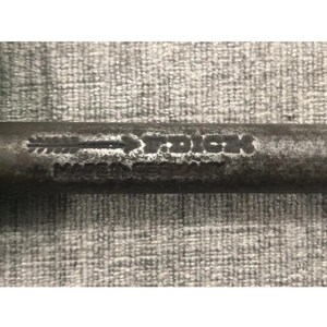May include: Close-up of a weathered metal object with the text "Made in Dick" visible. The object appears to be a tool or part of a larger mechanism, with a worn, aged appearance. The background is a textured, gray surface.