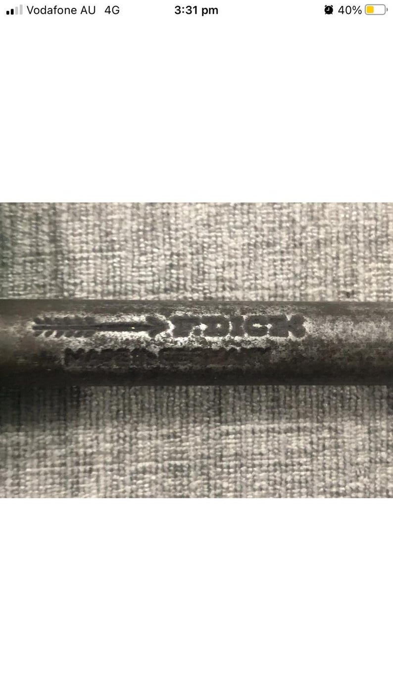 May include: Close-up of a weathered metal object with the text "Made in Dick" visible. The object appears to be a tool or part of a larger mechanism, with a worn, aged appearance. The background is a textured, gray surface.