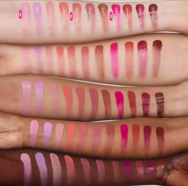 May include: A collection of lipstick swatches in various shades of pink, red, and brown, displayed on multiple arms with different skin tones. The swatches are labeled with names like "Bubblegum," "Cotton Candy," and "Coco Loco."