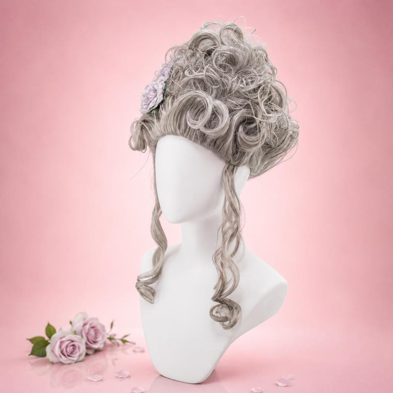 May include: A grey wig with elaborate curls and a small lavender flower accent, displayed on a white mannequin head. The wig features long, flowing curls and is set against a soft pink background. A few pink rose blossoms are at the base.