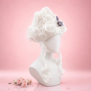 May include: A white wig with large curls and a grey rose detail is displayed on a white mannequin head and shoulders. The wig is styled in a historical fashion. Pink roses and petals are scattered on the pink background.