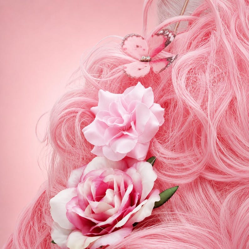 May include: Pink wig with a butterfly hair clip and two pink roses. The wig has long, wavy strands. The butterfly clip is light pink with a silver gem. The roses are light pink and white.