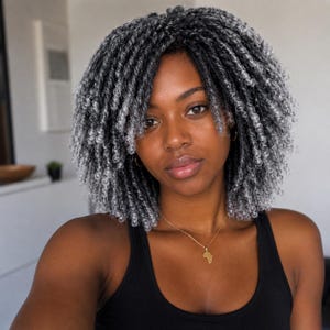 May include: A woman with gray and black curly hair and a black tank top. She is wearing a gold necklace with an Africa-shaped pendant. The image is a close-up shot of the woman's face and upper body.