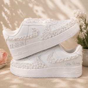 May include: A pair of white sneakers featuring pearl and rhinestone embellishments along the side swoosh and toe box. The top shoe displays the date 12-22-26, while the bottom shoe features the text Mrs. Wang in a cursive script font.