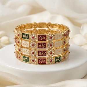 May include: A set of four gold-tone bangles featuring alternating rectangular and circular links. The rectangular links contain floral patterns in green, white, and maroon enamel, while the circular links are set with small clear stones.