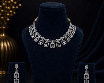 May include: A silver-toned necklace and matching drop earrings set featuring rectangular clear stones framed by smaller white stones. The necklace consists of a series of linked geometric rectangular segments, while each earring features three vertically aligned rectangular segments.