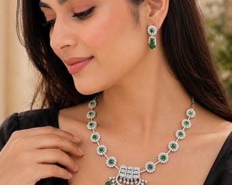 May include: A silver-toned necklace and matching earring set featuring circular links with clear white stones surrounding a central green stone. The necklace includes a large, semi-circular pendant with dangling green stones and white accents.