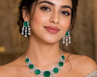 Op de afbeelding: Een ketting en bijpassende oorbellen met zeshoekige groene edelstenen omringd door kleine witte steentjes. De ketting bestaat uit een reeks van deze geschakelde zeshoekige stenen, terwijl de oorbellen een enkele zeshoekige steen hebben met drie hangende verticale strengen van kleinere ronde steentjes.
