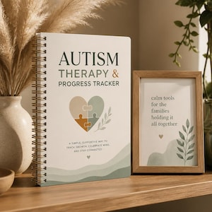 May include: A spiral-bound notebook titled Autism Therapy & Progress Tracker with a heart-shaped puzzle graphic. Beside it, a wooden frame displays the text: calm tools for the families holding it all together, featuring a small heart and leaf design.
