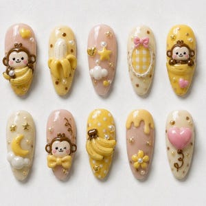 Könnte beinhalten: Ein Set aus zehn künstlichen Fingernägeln mit verschiedenen 3D-Applikationen wie Comic-Affen, gelben Bananen, rosa Herzen, Sternen, Monden, Wolken und kleinen weißen Perlen. Die Grundfarben sind Creme, Hellrosa und Gelb mit Punkten.
