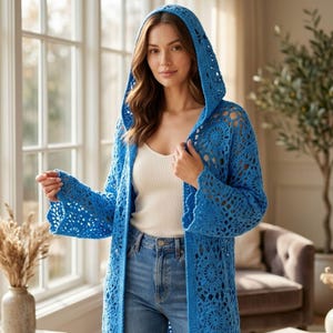 May include: A bright blue crochet hooded cardigan featuring an intricate openwork floral pattern, long sleeves with scalloped edges, and a relaxed open front design, worn over a simple white tank top and classic blue denim jeans.
