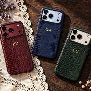 May include: Three smartphone cases with a textured lizard-skin pattern in burgundy, navy blue, and dark green. Each case features gold-colored embossed initials: BD on the burgundy case, GM on the navy case, and A.C on the green case.