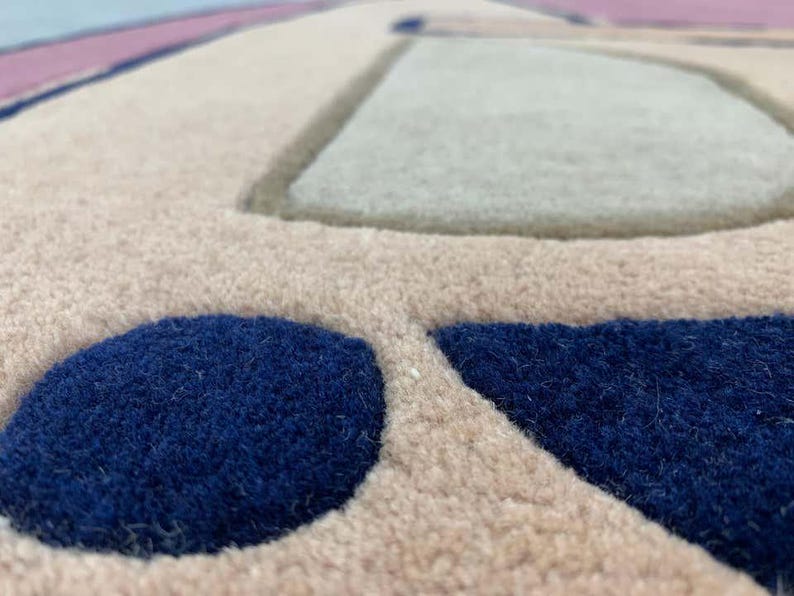 May include: A tufted rug featuring a beige base with raised, textured geometric shapes in deep navy blue and light gray. The surface has a thick, plush pile construction with distinct color-blocked sections and clean, defined edges throughout.