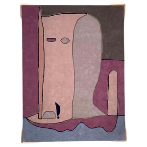May include: A rectangular area rug featuring an abstract, stylized figure in shades of dusty pink, mauve, and grey. The design includes bold black outlines, a dark purple background, and a light blue base, creating a flat, graphic composition.