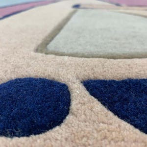 May include: A tufted rug featuring a beige base with raised, textured geometric shapes in deep navy blue and light gray. The surface has a thick, plush pile construction with distinct color-blocked sections and clean, defined edges throughout.