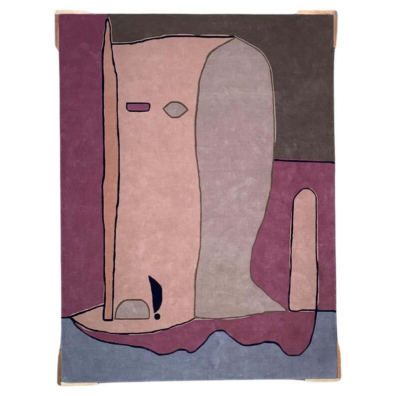 May include: A rectangular area rug featuring an abstract, stylized figure in shades of dusty pink, mauve, and grey. The design includes bold black outlines, a dark purple background, and a light blue base, creating a flat, graphic composition.