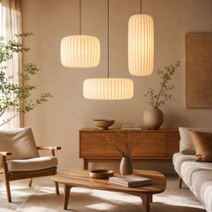 May include: Three white ribbed pendant lights with cylindrical and disc shapes hang from the ceiling. The lights emit a warm glow, illuminating the room. Each fixture features a textured, vertical-striped surface and is suspended by a thin cord.