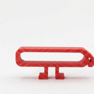 May include: A red, textured, elongated loop-shaped object with a flat base featuring two small, rectangular feet. The structure has a rounded, closed end on the right side and a continuous, hollow, horizontal opening through the center of the frame.