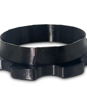 May include: A black, circular, gear-shaped component with a smooth, raised cylindrical collar extending from the center. The object features a series of evenly spaced, rounded teeth around its outer perimeter and has a glossy, solid finish.