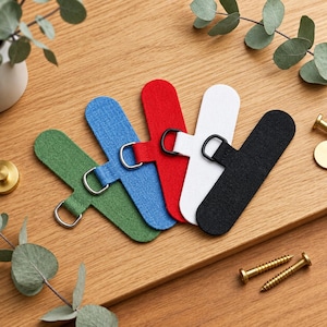 May include: Five fabric wall hanging tabs in green, blue, red, white, and black. Each elongated tab features a rounded end and a metal D-ring attached to a small loop. The tabs are arranged in a fan shape, showcasing their textured material.