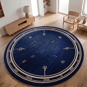 May include: A large circular rug in deep navy blue featuring a cream-colored border with geometric line patterns and symbols. The central field is solid navy blue with four symmetrical linear motifs arranged in a compass-like configuration.