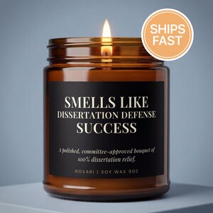 May include: A lit brown glass candle jar with a black label that reads "SMELLS LIKE DISSERTATION DEFENSE SUCCESS." The candle has a "SHIPS FAST" sticker. The text below the title reads "A polished, committee-approved bouquet of 100% dissertation relief."