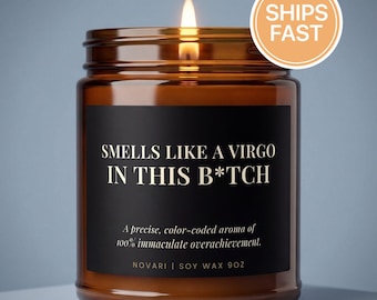Pode incluir: Uma vela acesa num frasco de vidro âmbar com um rótulo preto. O rótulo diz: SMELLS LIKE A VIRGO IN THIS B*TCH, A precise, color-coded aroma of 100% immaculate overachievement. NOVARI | SOY WAX 9OZ. A vela tem uma chama visível no topo.