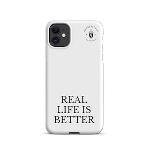 May include: A white smartphone case featuring the black text REAL LIFE IS BETTER printed in the lower center. Near the top right corner, a small circular logo displays a coffee cup icon with the text PAUKERSTYLE FOR SURVIVORS around it.
