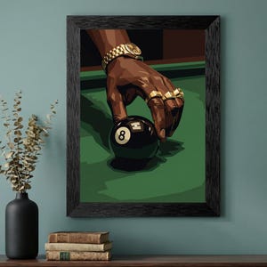 May include: Framed art print featuring a hand with gold rings and a watch, holding a black 8-ball on a green pool table. The artwork has a dark, stylized aesthetic with a black frame.
