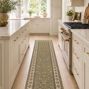 May include: A long, rectangular runner rug featuring a sage green central field with an intricate floral pattern in shades of cream, red, and dark green. The rug is framed by a decorative border with repeating floral motifs and dark trim.
