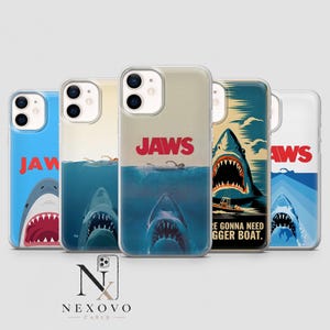 Op de afbeelding: Vijf doorzichtige smartphonehoesjes met diverse grafische ontwerpen in het thema van de film Jaws. Elk hoesje toont een haai, water en het rode Jaws-logo. Eén hoesje bevat de tekst You're gonna need a bigger boat bij een haai en een boot.
