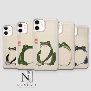 May include: Five clear phone cases featuring various illustrations of frogs in a traditional ink-wash style. Some frogs are depicted sitting with small bowls, while others are shown in profile. Each case includes a small red square with Japanese text.