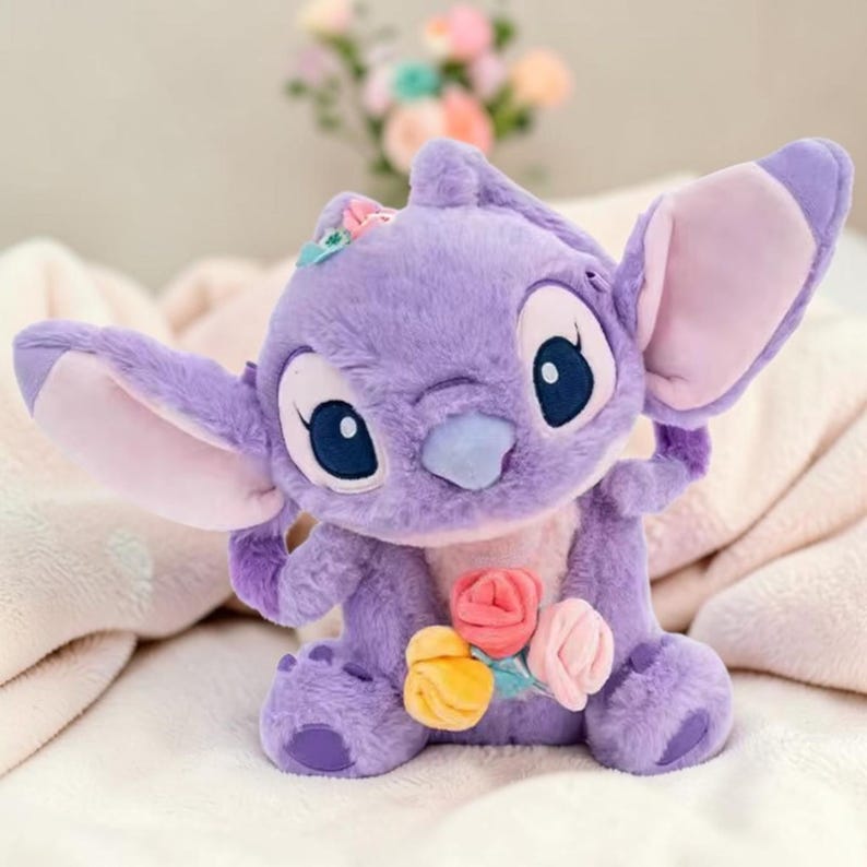 Puede incluir: Un peluche morado de un personaje de dibujos animados con grandes orejas y ojos azules, sosteniendo un ramo de flores. El juguete tiene una peque&ntilde;a flor en la cabeza. El fondo es borroso.