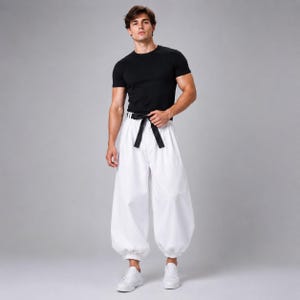 Könnte beinhalten: Ein schwarzes kurzärmeliges T-Shirt kombiniert mit einer locker sitzenden weißen Hose mit hoher Taille, einem vorne gebundenen schwarzen Stoffgürtel und gerafften elastischen Bündchen an den Knöcheln, getragen mit schlichten weißen Sportschuhen.