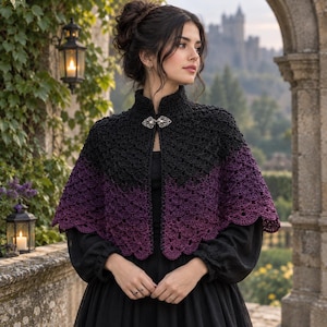 May include: A crochet capelet featuring a black upper section that transitions into a deep purple lower section with a scalloped hem. The garment is secured at the neckline with a silver-toned metal clasp featuring intricate filigree detailing.