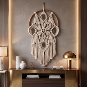 May include: A circular macrame wall hanging featuring off-white knotted cord arranged in a symmetrical star pattern. The design includes dark brown wooden leaf-shaped accents, small metallic beads, and a central star, all suspended from a wooden hoop.