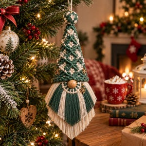 May include: A macrame gnome ornament featuring a conical hat in dark green and cream cord with a diamond pattern, a round wooden nose, and a long, layered fringe beard in alternating dark green and cream strands, topped with a small loop.