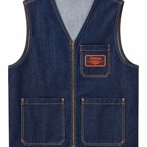 May include: A dark blue denim vest with a V-neckline and a full-length front zipper. The vest features two large lower patch pockets with copper-colored rivets and a single chest pocket with a rectangular orange and black Dickies brand patch.