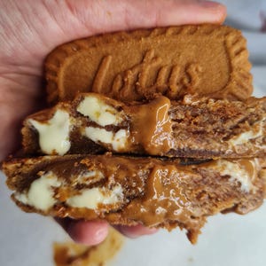 Peut inclure: Gros plan d'un sandwich au biscuit. Le biscuit supérieur est estampillé du mot "Lotus". Le sandwich a une garniture blanche crémeuse et une pâte à tartiner couleur caramel. Le biscuit est de couleur brun doré.