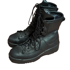 May include: A pair of black leather tactical boots featuring a high-top design, reinforced toe caps, and a lace-up closure system with metal eyelets. The interior lining is a grey textured fabric, and the boots have thick, durable rubber soles.