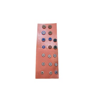 May include: A rectangular peach-colored card displaying a collection of twenty-two small circular buttons arranged in rows. The buttons vary in color, including shades of blue, brown, white, and black, and feature different patterns and textures.