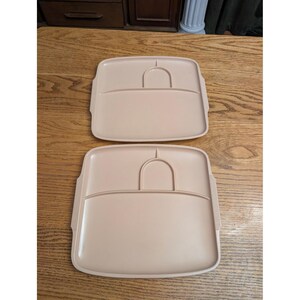 May include: Two light beige plastic serving trays with a square shape and rounded corners. Each tray features a large main compartment and a smaller arched section at the top, with textured grip handles on the left and right sides of the tray.