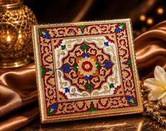 May include: A square decorative box featuring an intricate gold-toned frame and a central panel with a white background. The surface is adorned with embossed floral patterns in vibrant red, green, blue, and yellow enamel paint accents.