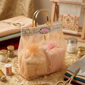 May include: A peach-colored sheer organza gift bag with gold metal handles, featuring a silver embroidered trim and a pink lotus flower emblem. The bag contains two small fabric pouches and has a small rectangular tag reading Handcrafted with Love.