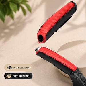 May include: A car handbrake cover featuring a red carbon fiber pattern on the top section and solid black material on the sides, joined by black stitching. The cover is shown in two pieces, with one section hovering above the installed handle.