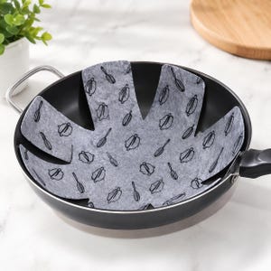 May include: A black metal frying pan with a grey felt pan protector insert. The protector is star-shaped with eight petals and features a repeating black line art pattern of kitchen whisks and cooking pots printed across the grey surface.