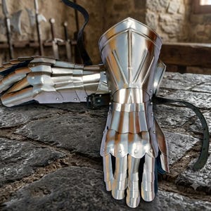 May include: A pair of polished steel gauntlets featuring articulated finger plates, a reinforced cuff, and black leather straps for secure fastening. The metal armor pieces are constructed with overlapping plates designed to protect the hand and wrist.