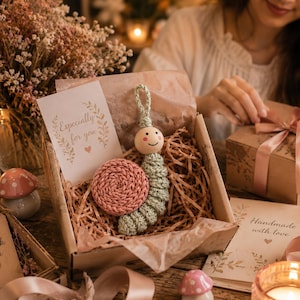 May include: A gift box containing a handmade crochet caterpillar toy, a pink crocheted circle, and a card that reads "Especially for you." The box also contains a gift wrapped in brown paper with a pink ribbon. A "Thank you" tag is visible.
