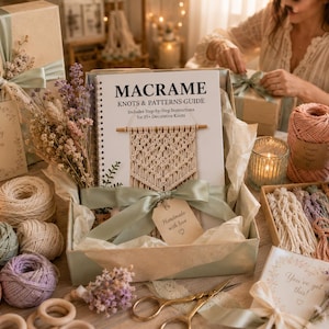 May include: A macrame craft kit in a gift box featuring a spiral-bound Macrame Knots & Patterns Guide, assorted pastel cotton cords, wooden rings, dried flowers, and gold scissors. The box includes a tag labelled Handmade with love.